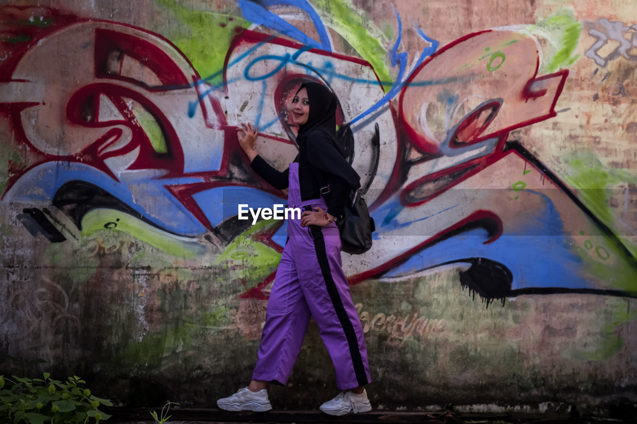 Full length of teenage women standing against graffiti wall