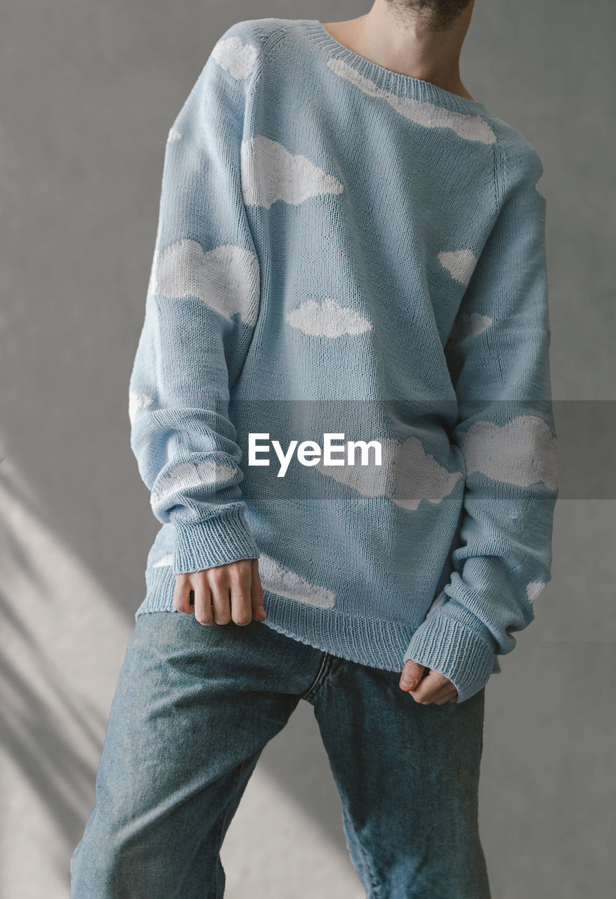 Midsection of man in a sweater with clouds standing against wall