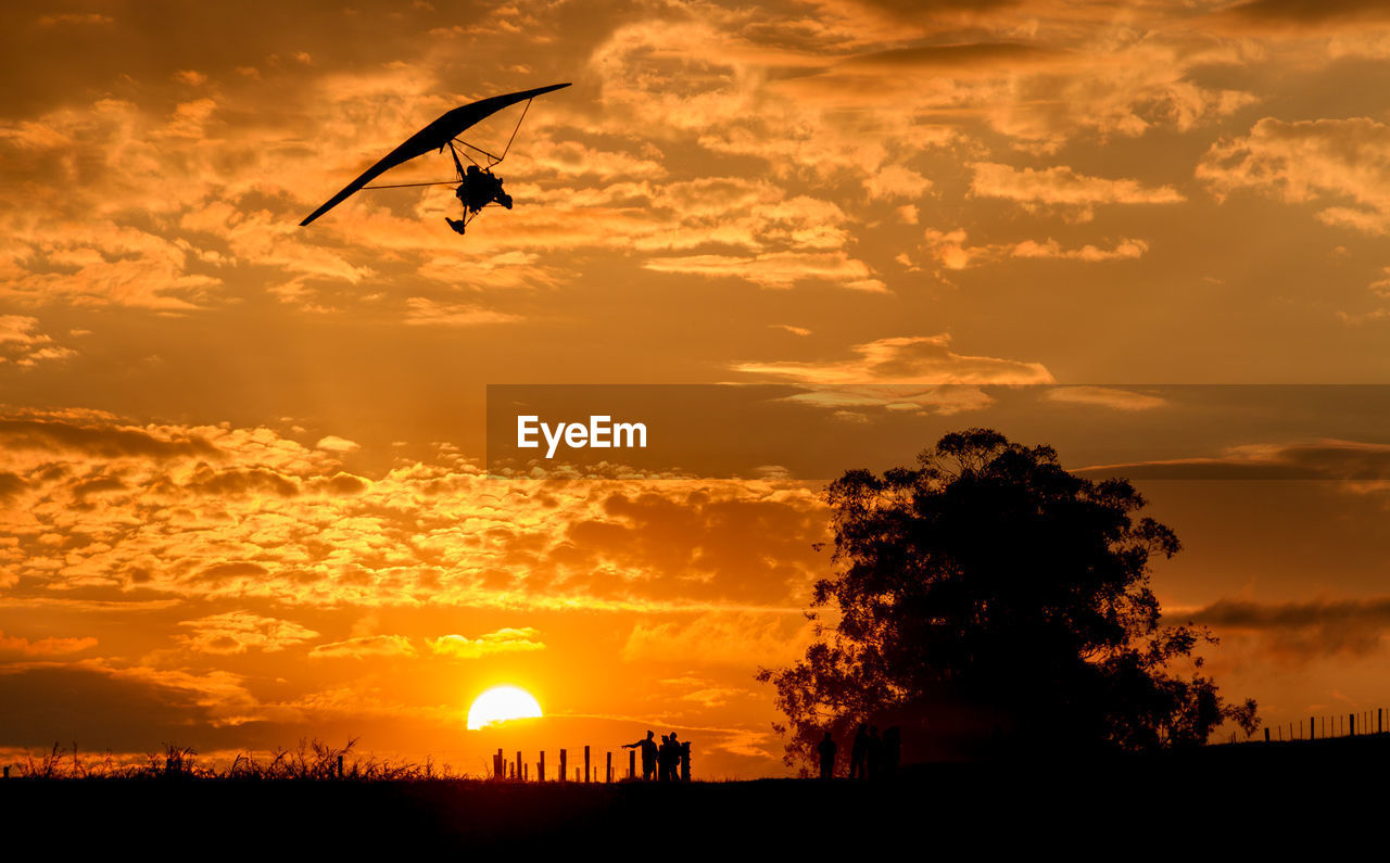 Low angle view of silhouette person hang-gliding against dramatic sky during sunset