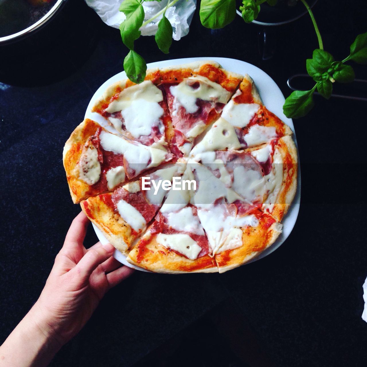 Cropped image of hand holding plate with pizza on table
