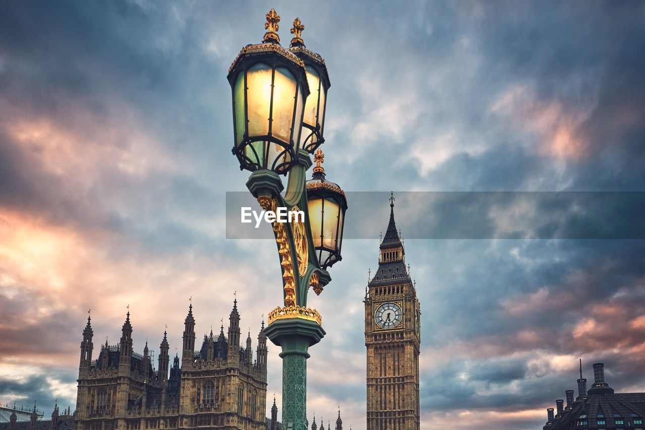 Low angle view of illuminated street light with big ben and houses of parliament against cloudy sky