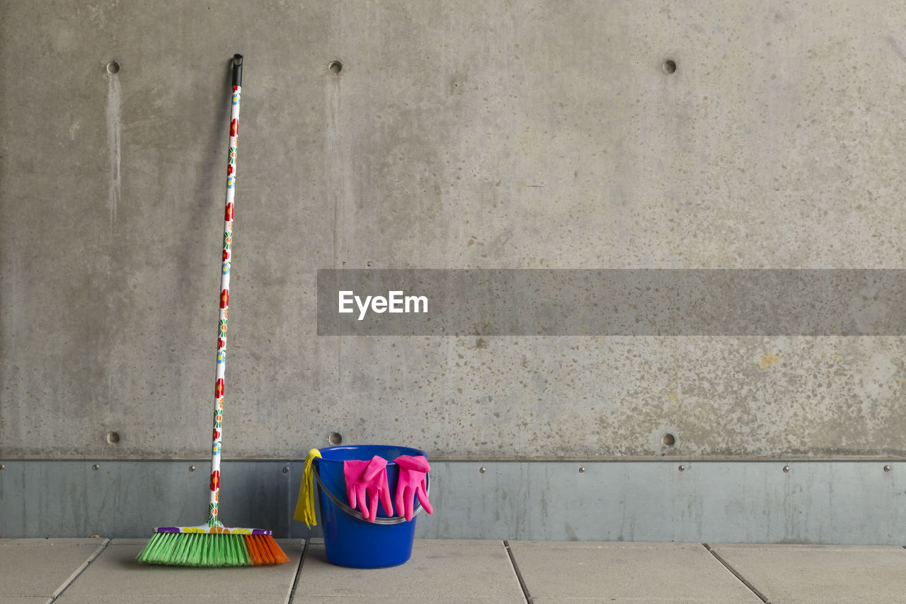 Multi colored broom with bucket on floor against wall