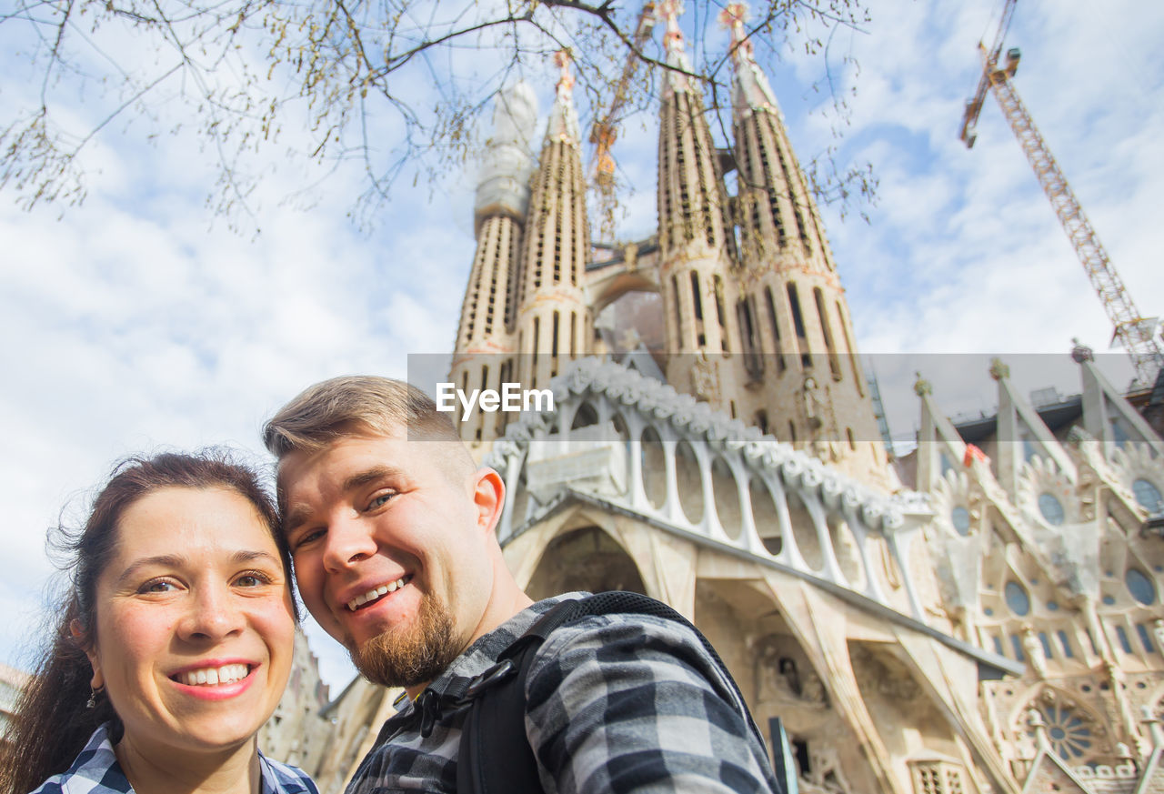 PORTRAIT OF SMILING FRIENDS AGAINST BUILDINGS