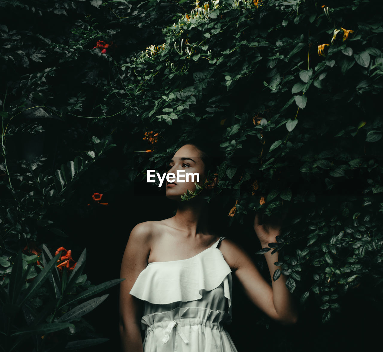 Young woman looking away while standing against plants