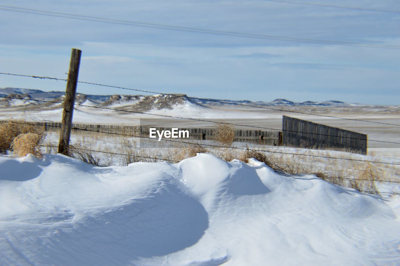 Barbed wire on snow covered field against sky