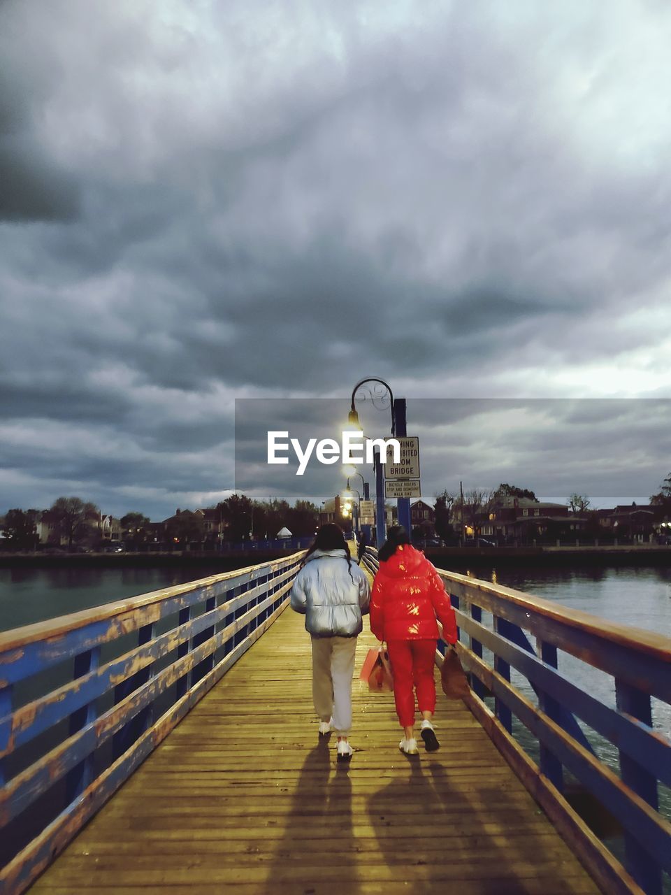 REAR VIEW OF PEOPLE WALKING ON RAILING AGAINST SKY