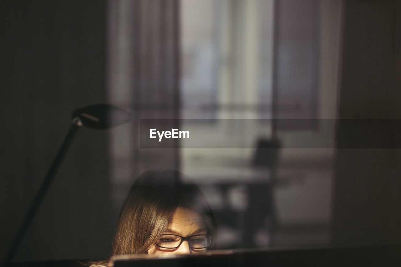 Businesswoman wearing eyeglasses using computer seen through glass at office