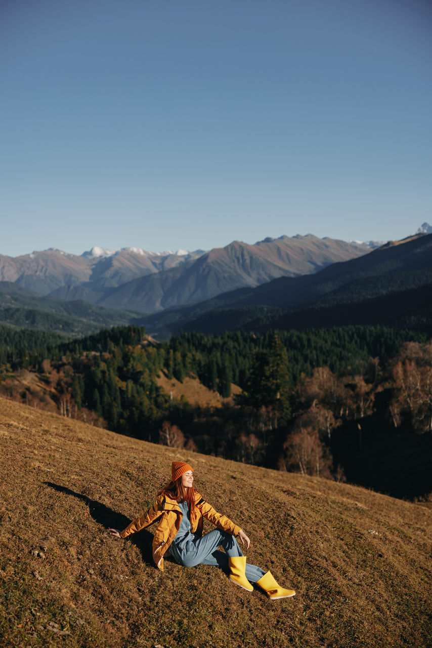 rear view of woman sitting on mountain against clear sky