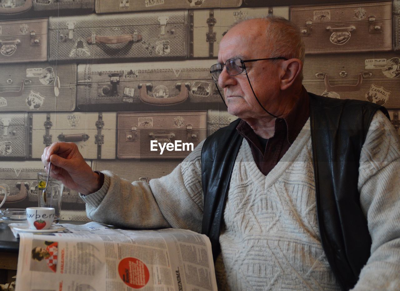 Senior man reading newspaper while stirring coffee in cafe