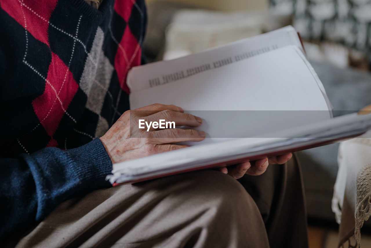 Midsection of senior woman reading book in home