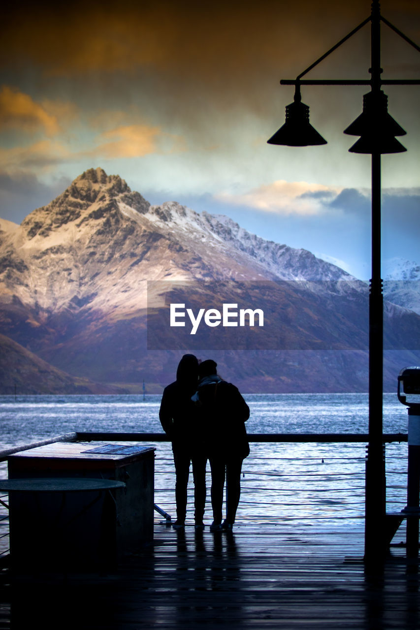 Silhouette of couples standing on queenstown harbor pier against beautiful mountain scene