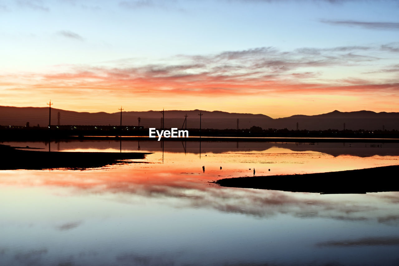 sky, reflection, water, sunset, cloud, dawn, beauty in nature, nature, scenics - nature, tranquility, sea, tranquil scene, no people, horizon, evening, environment, mountain, orange color, outdoors, landscape, silhouette, idyllic, sunlight, afterglow, dramatic sky, architecture, travel destinations, sun, non-urban scene