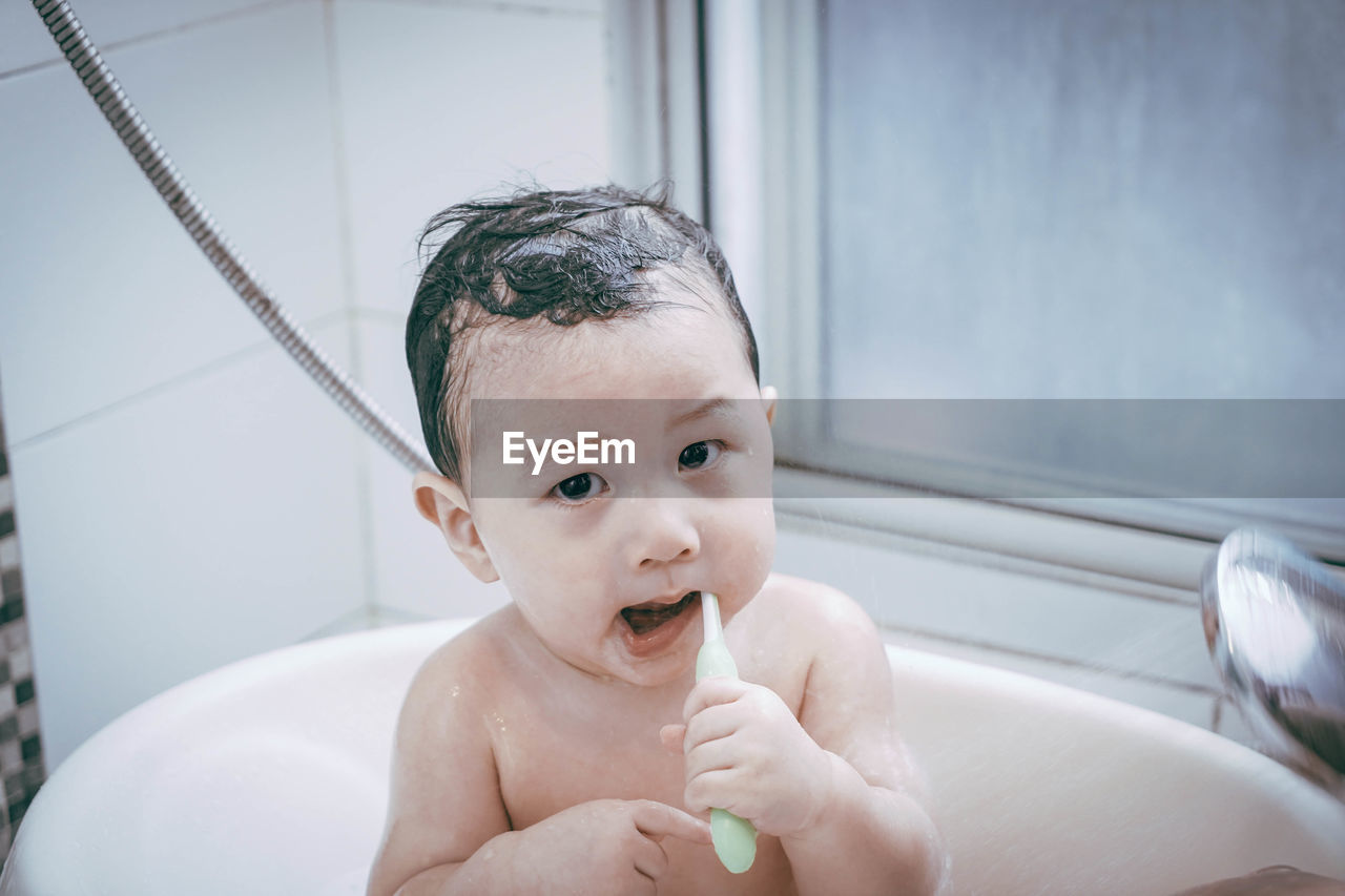 Portrait of cute baby boy brushing teeth in bathtub