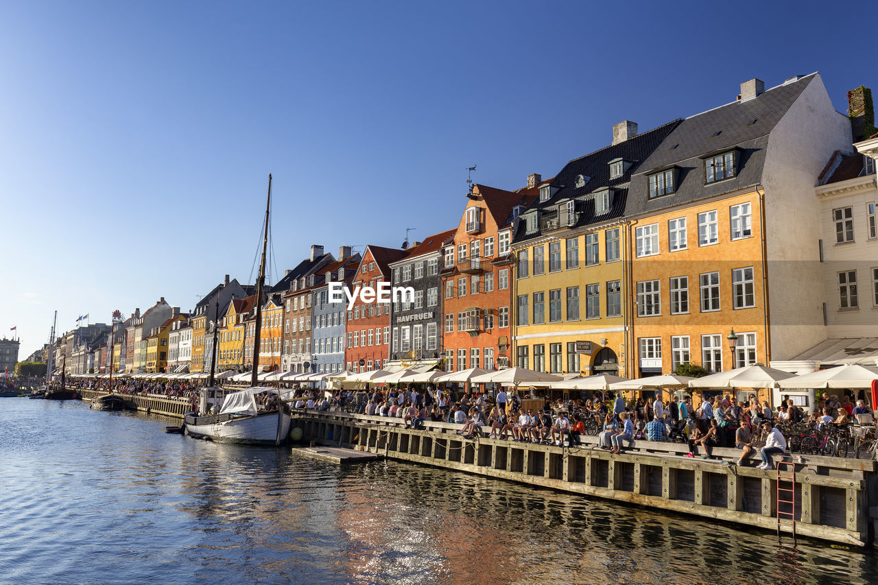 PEOPLE ON RIVER BY BUILDINGS AGAINST SKY