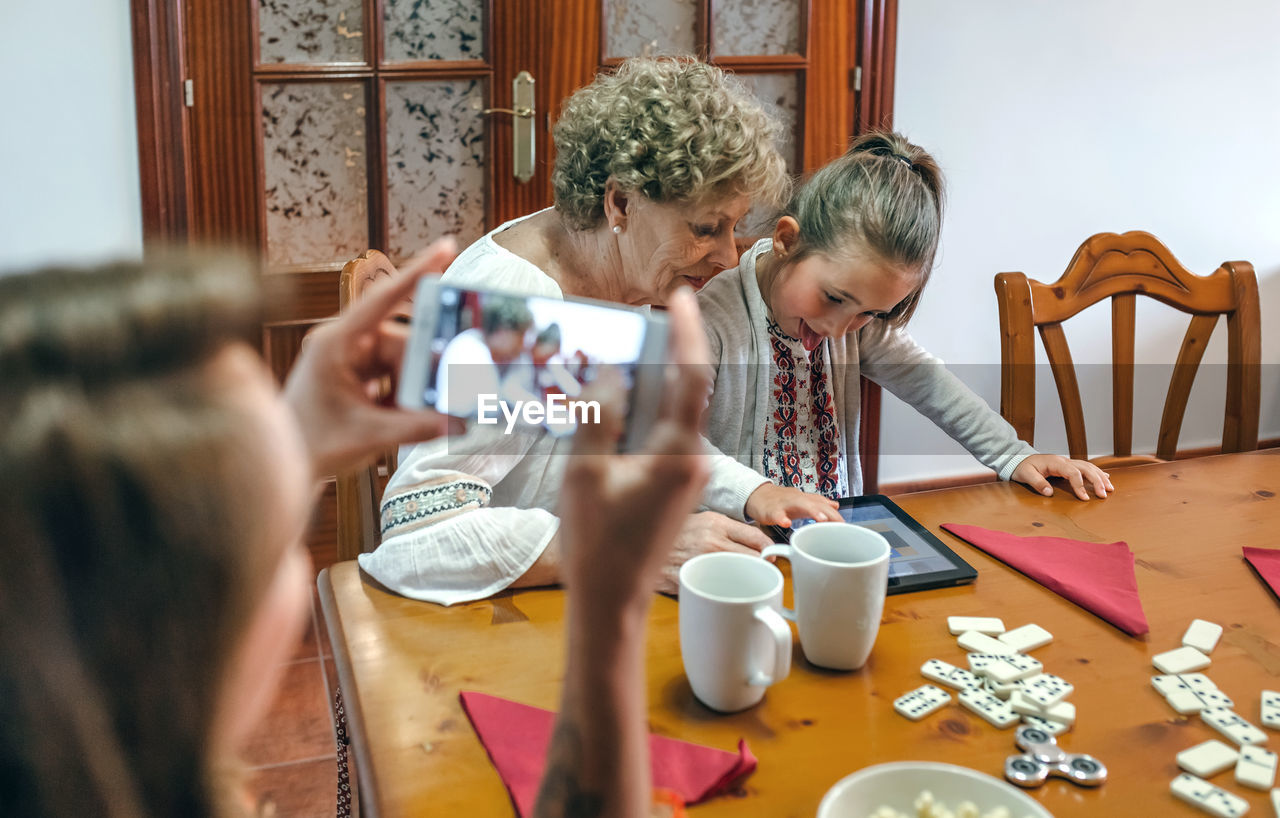 Woman photographing family playing mobile game at table