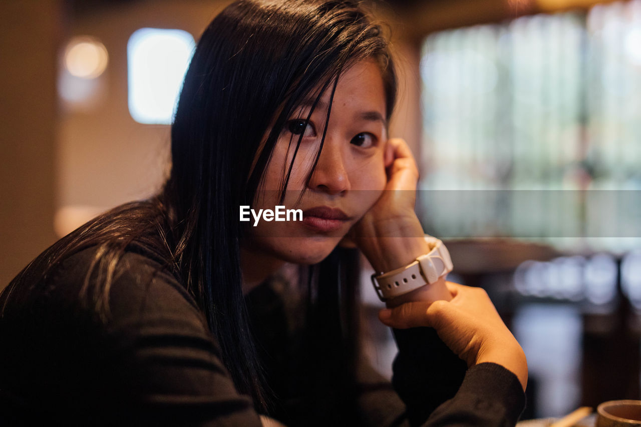 Close-up portrait of woman with hand on chin in cafe