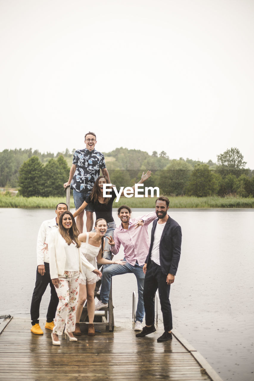 Portrait of cheerful multi-ethic friends standing on jetty over lake during holiday