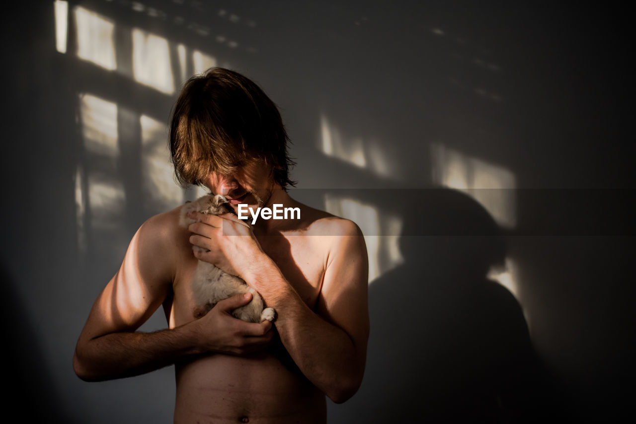 Close-up of shirtless young man carrying dog against wall