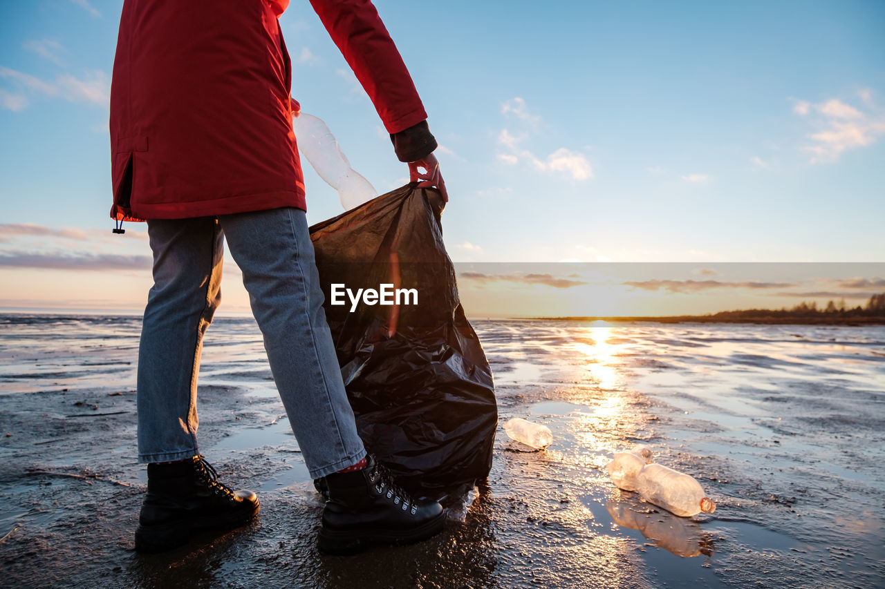 A woman cleans the bank of plastic bottles and puts the trash in a garbage bag