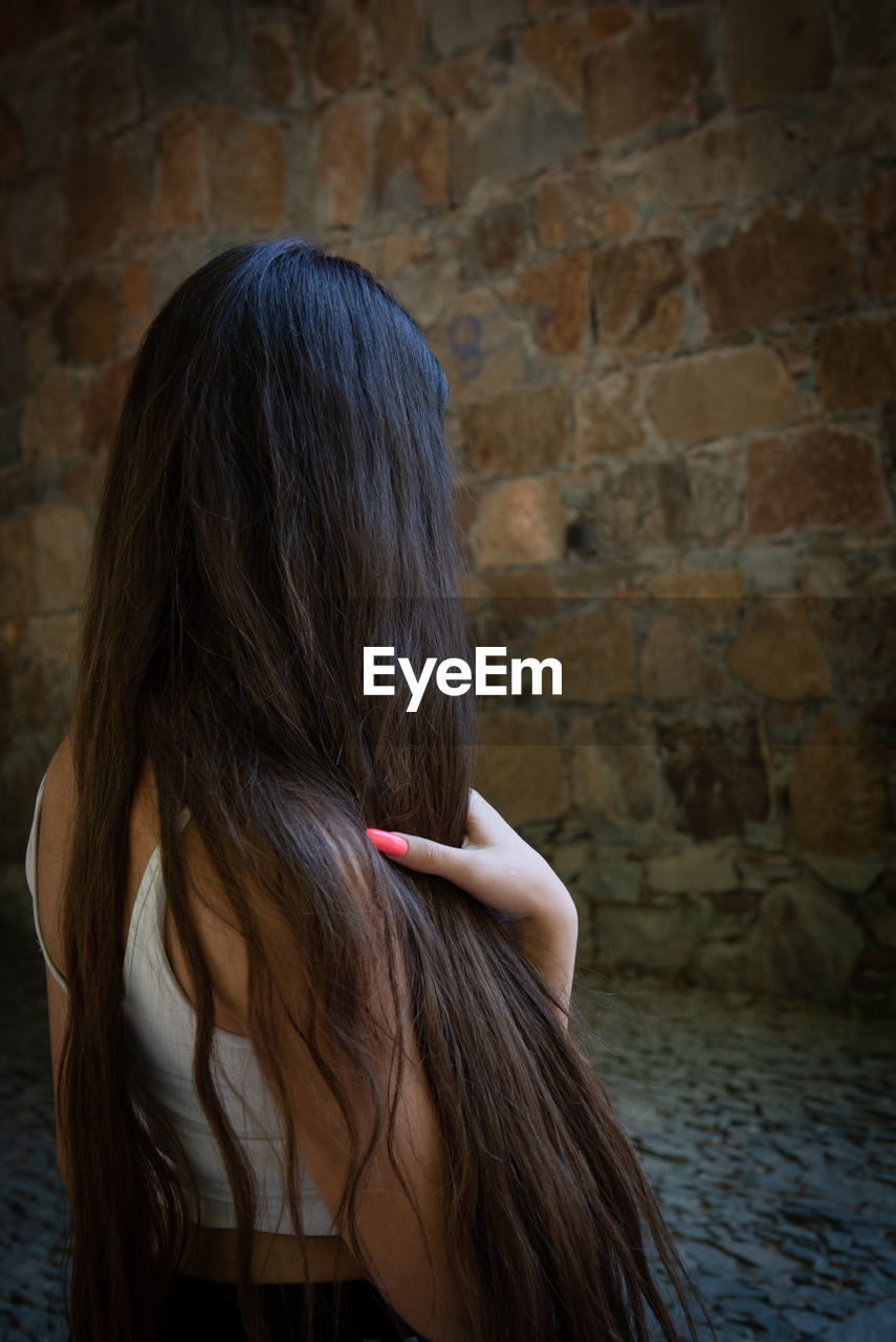 Rear view of woman holding hair standing against wall