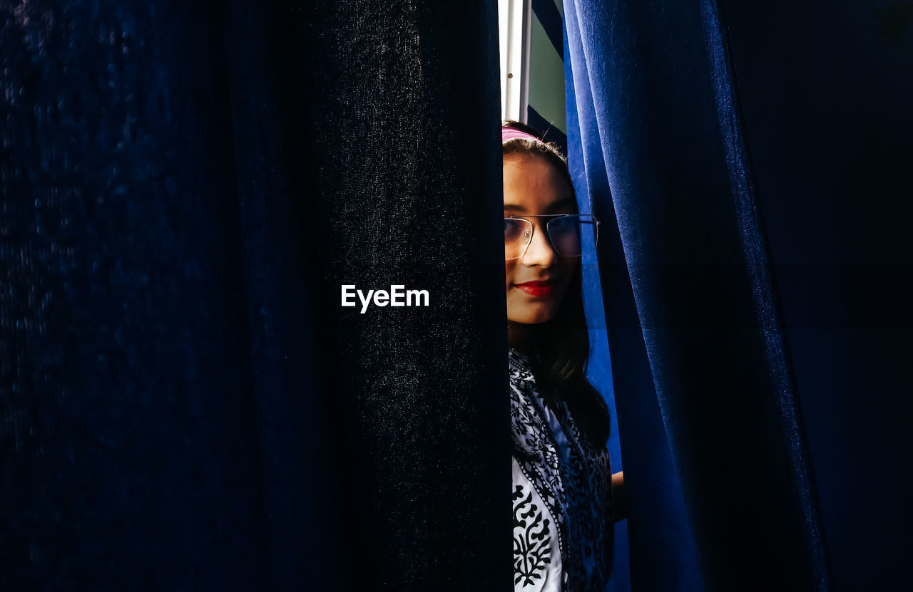 Portrait of smiling teenage girl seen through curtains