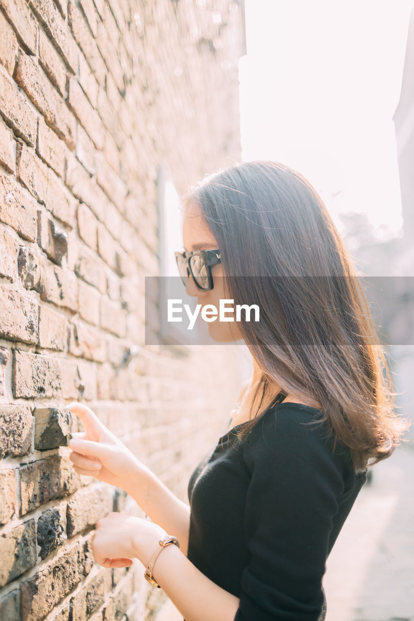 Side view of young woman standing by wall