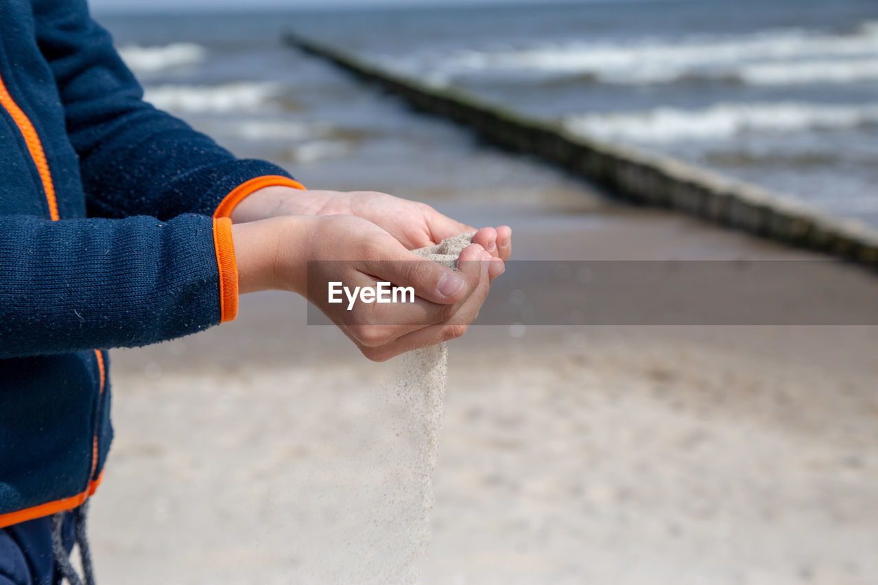 MIDSECTION OF PERSON HOLDING SUNGLASSES ON BEACH