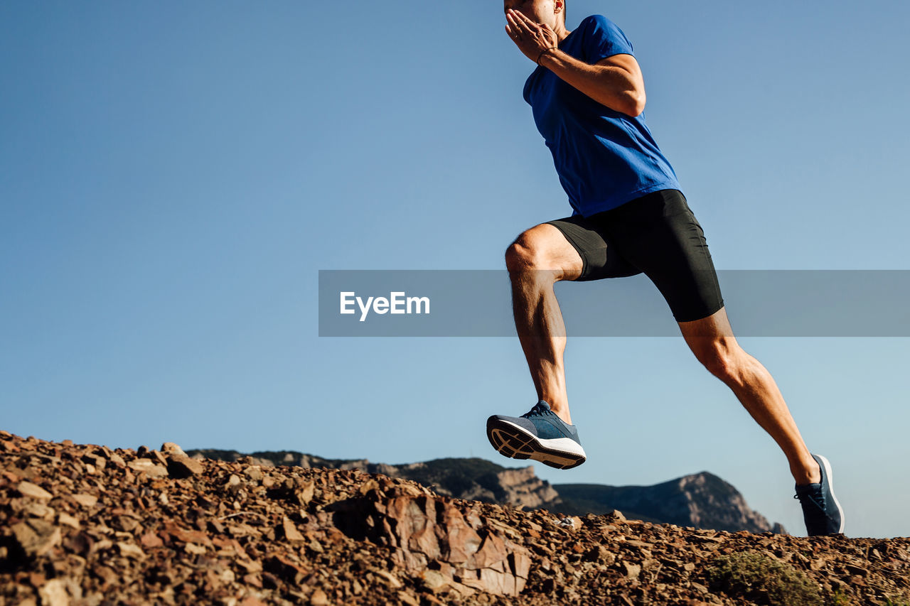 Low angle view of man jumping on rock against clear sky