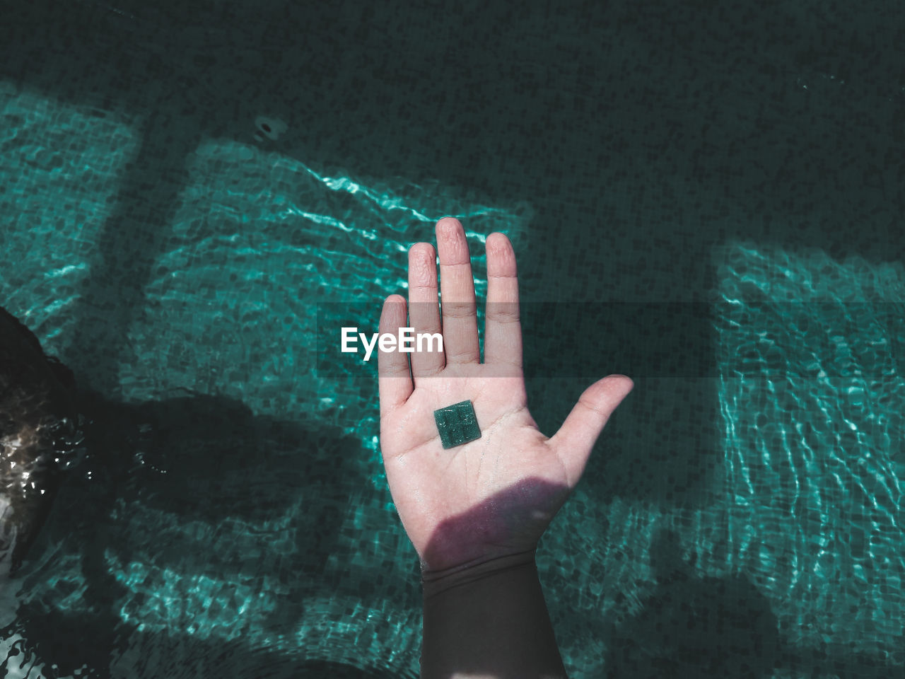 Close-up of hand touching water in swimming pool