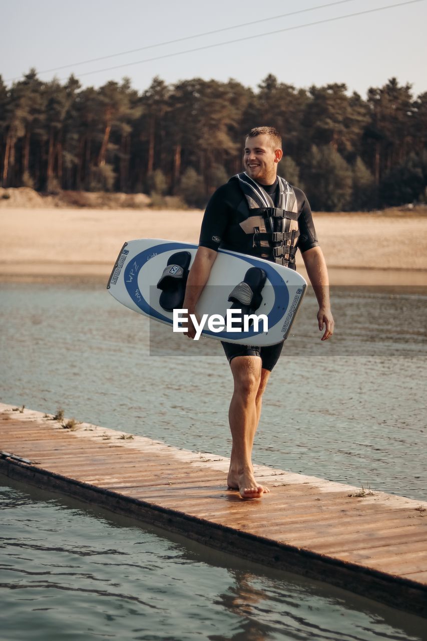 Full length of young man holding surfboard walking on pier