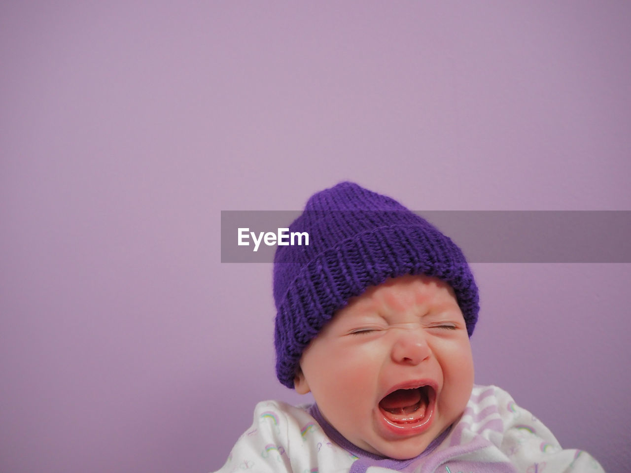 Close-up of crying baby against purple background