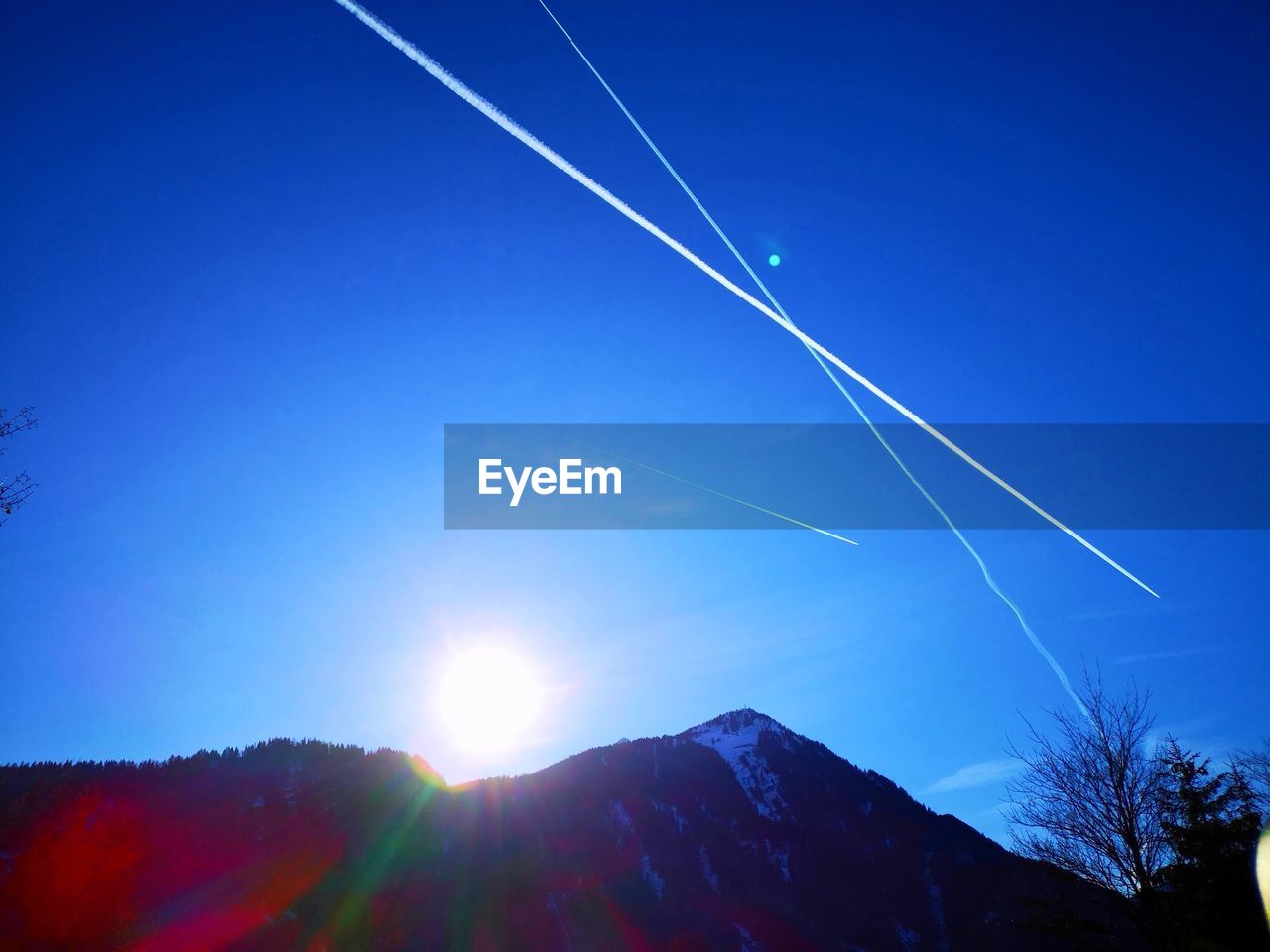 LOW ANGLE VIEW OF VAPOR TRAIL OVER SILHOUETTE MOUNTAIN AGAINST BLUE SKY