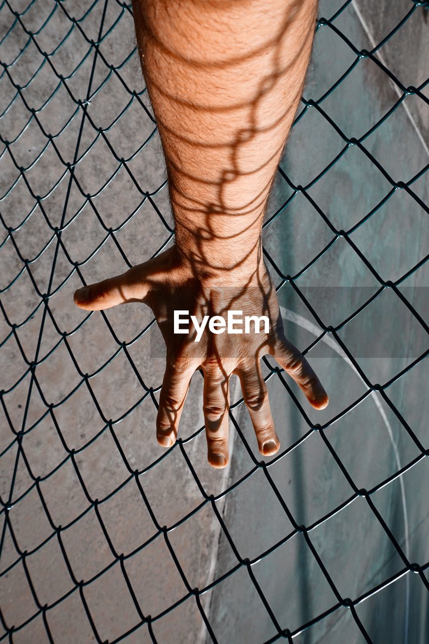 Hand with shadow shapes grabbing a metallic fence