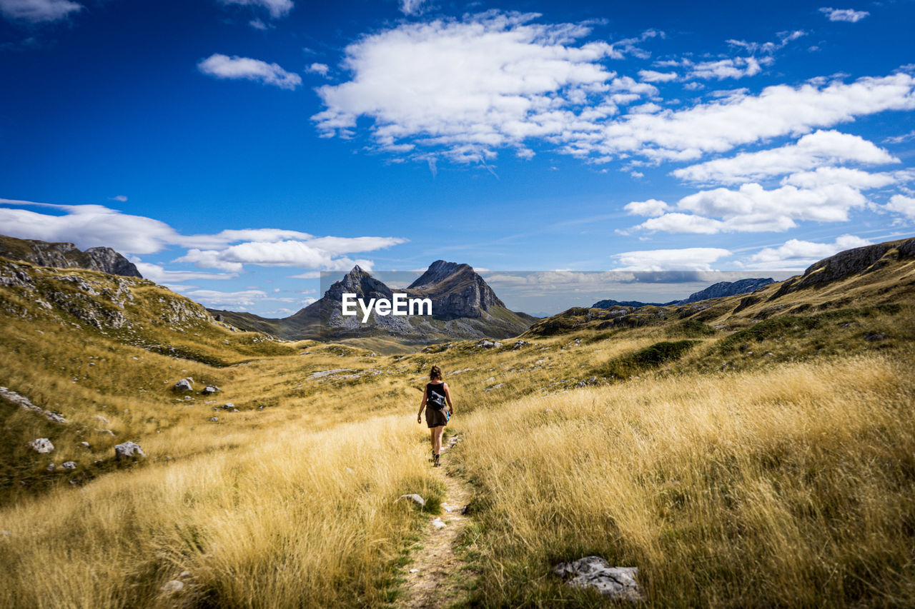 Rear view of woman walking on field against sky with mountains