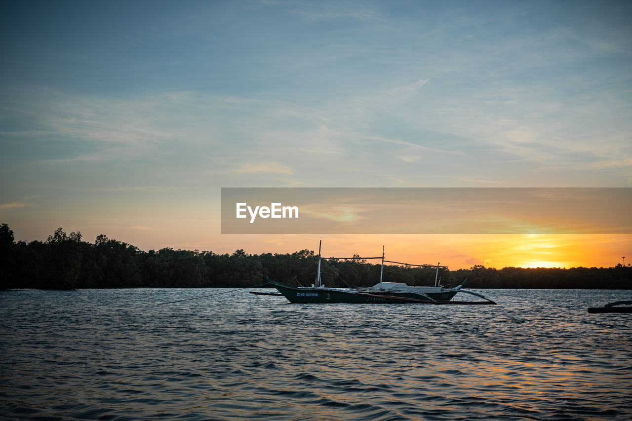 water, sky, sunset, reflection, nautical vessel, transportation, evening, dusk, nature, cloud, mode of transportation, sea, beauty in nature, ship, scenics - nature, tranquility, horizon, vehicle, tranquil scene, boat, no people, travel, outdoors, shore, idyllic, sunlight, ocean, sailboat, tree, silhouette, sailing, non-urban scene, travel destinations, environment, sun, watercraft