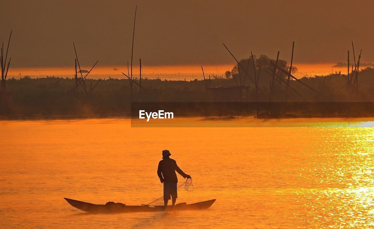 Silhouette man fishing in river against sky during sunset
