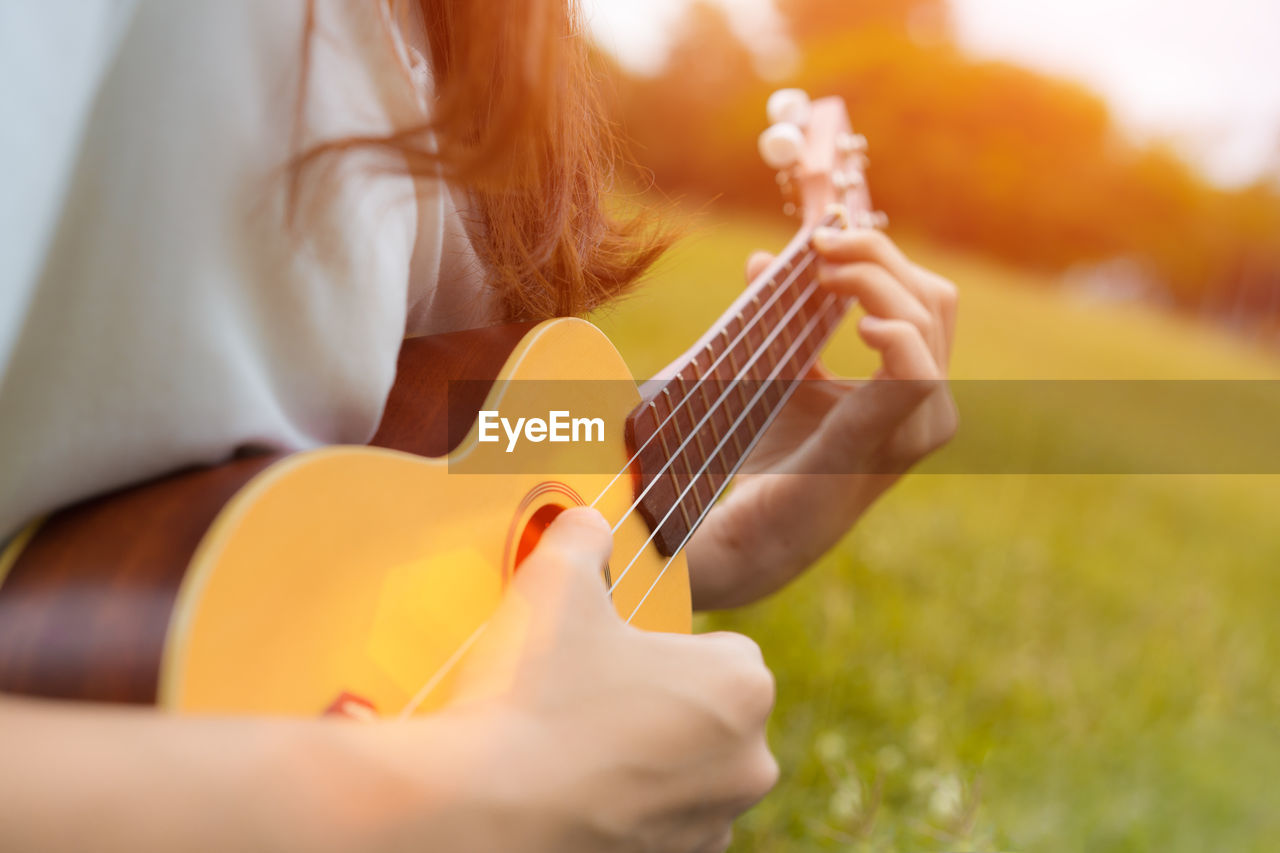 Midsection of woman playing ukulele on grass