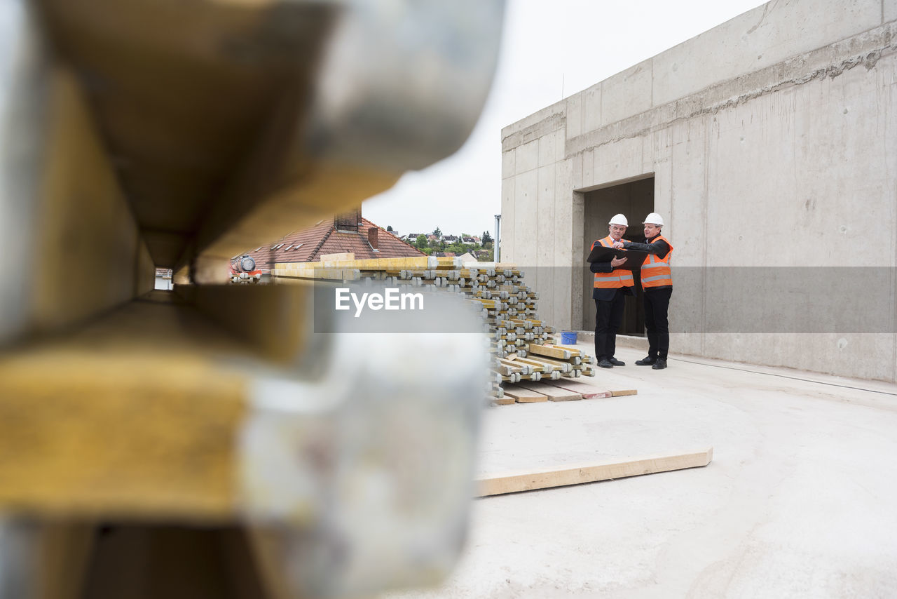 Two men wearing safety vests talking on construction site