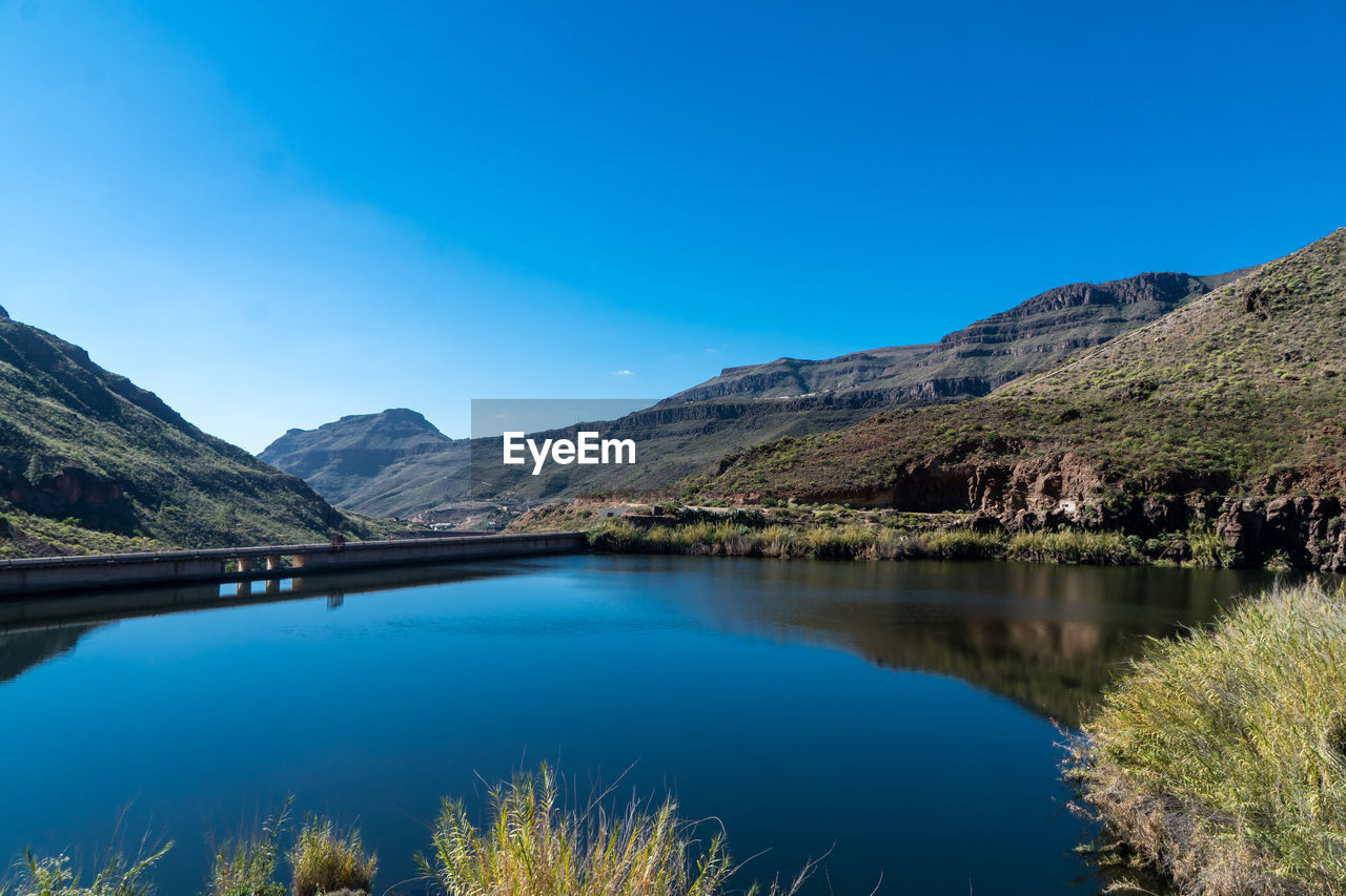 Scenic view of lake and mountains against clear blue sky