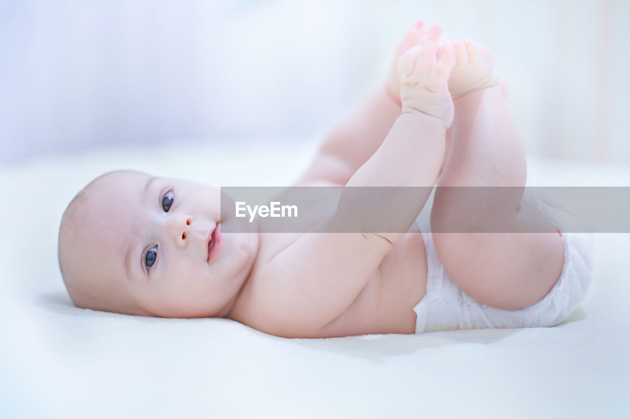 Portrait of shirtless cute baby boy lying on bed at home