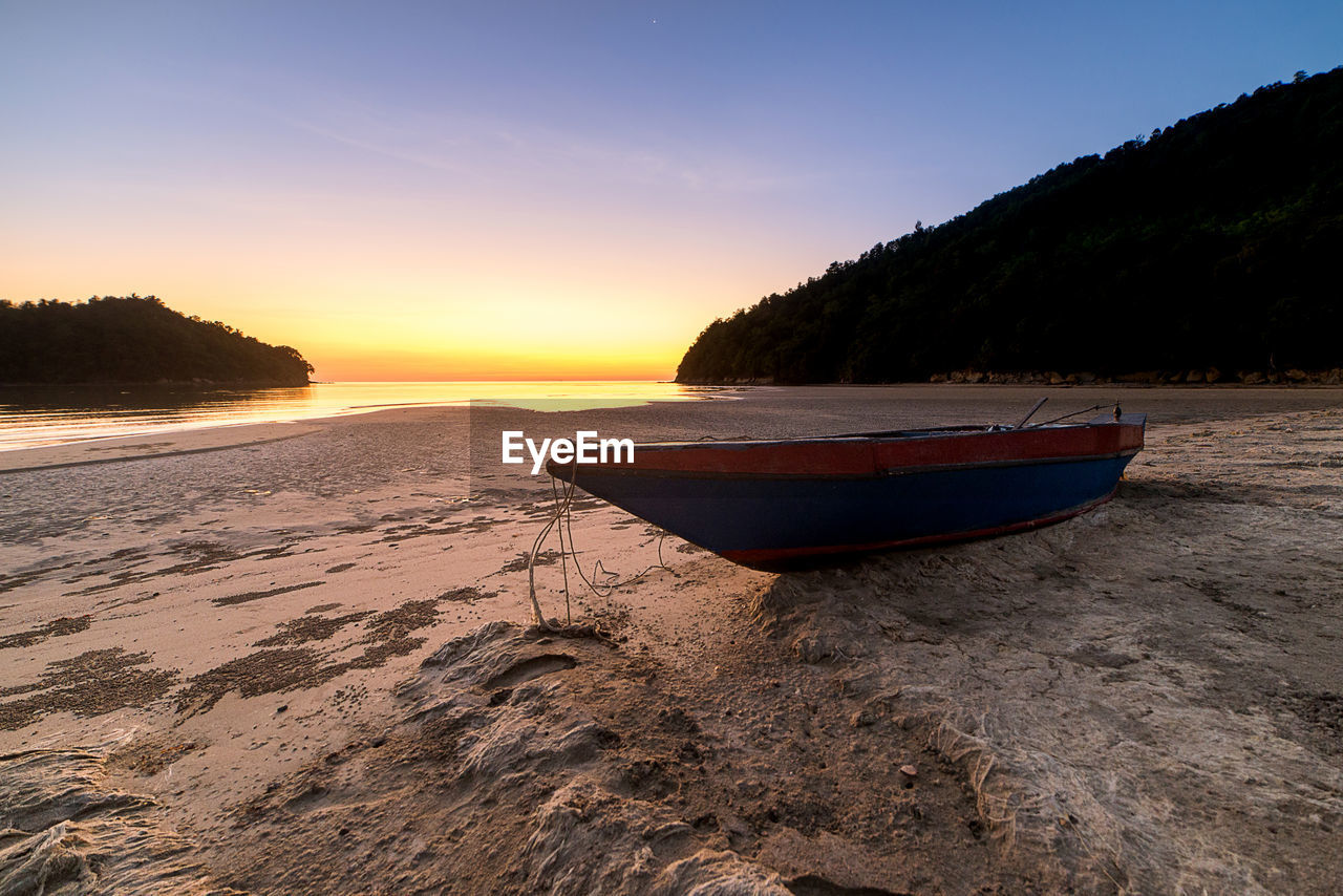 BOAT MOORED ON SHORE AGAINST SKY DURING SUNSET