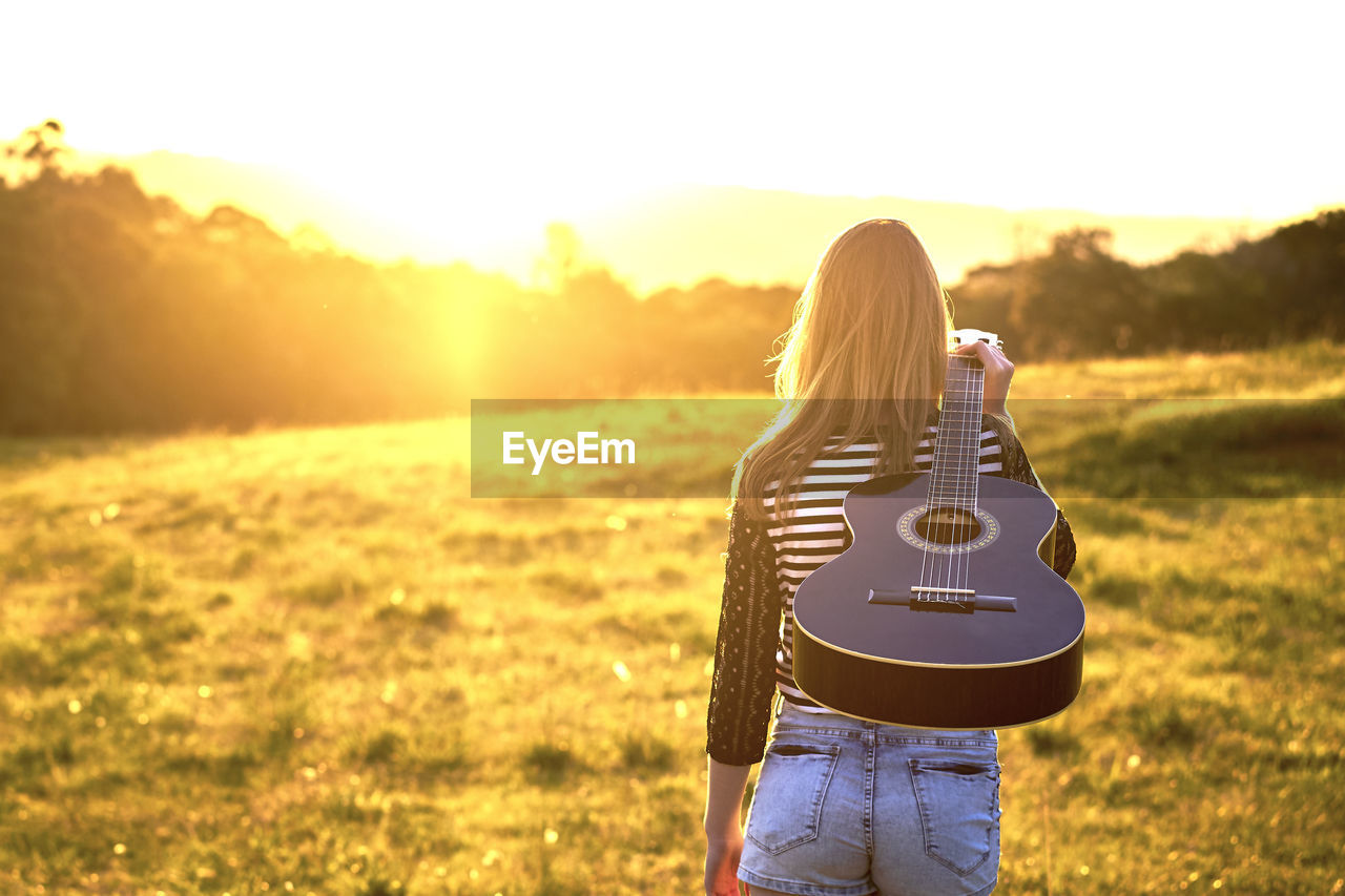 Rear view of woman carrying guitar on field