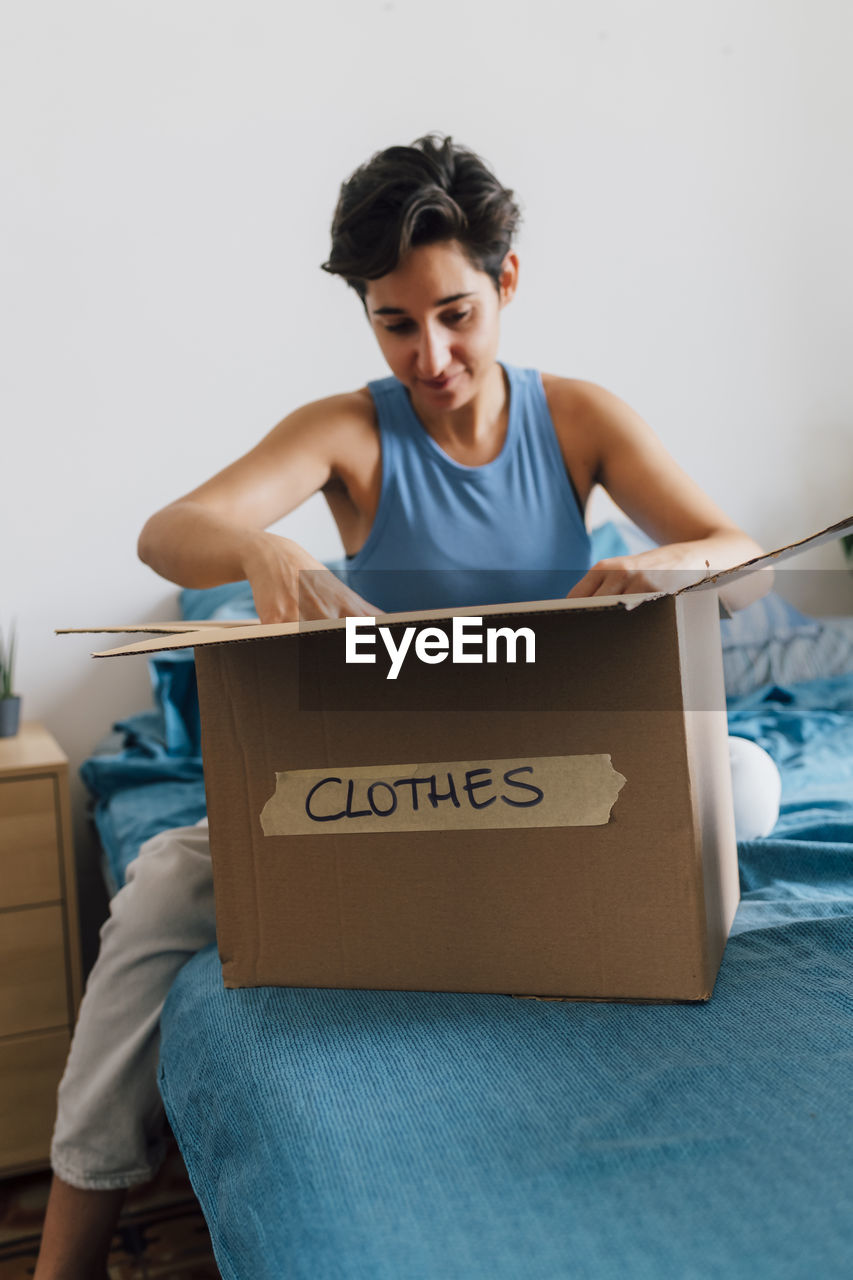 Young woman packing donation box in bedroom