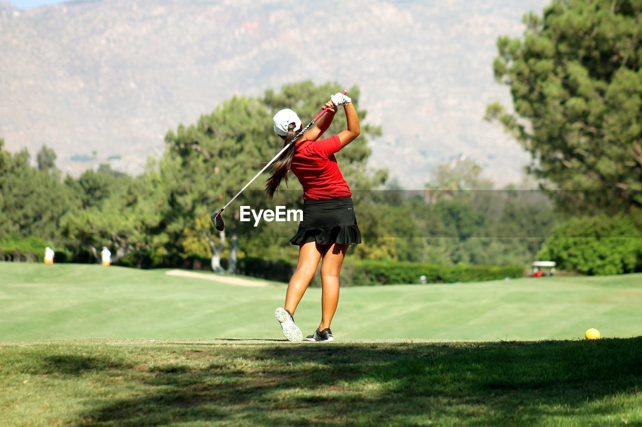 Rear view of woman in sports clothing swinging at golf course