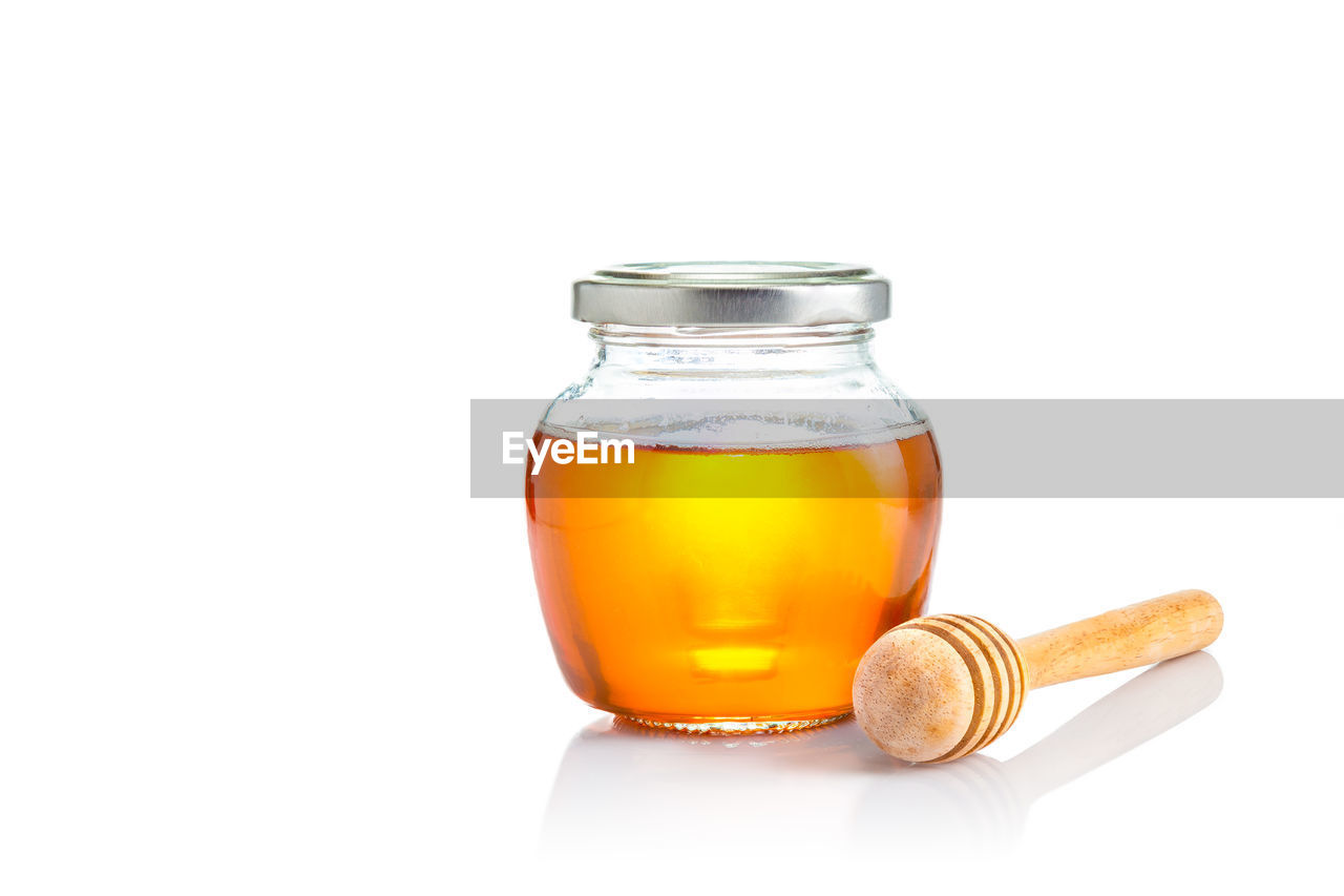 Honey in glass jar with wooden honey dipper on white background