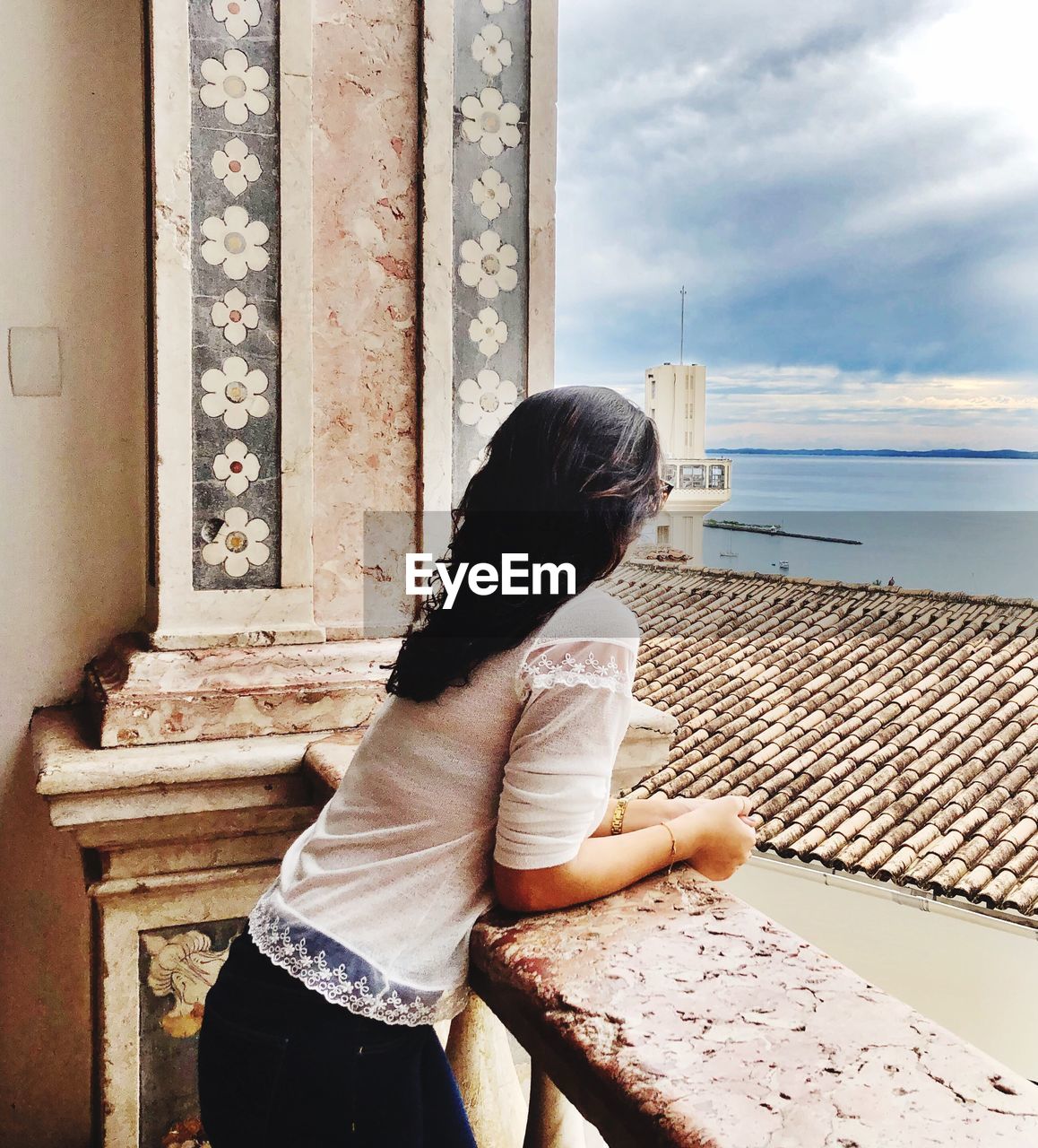 Side view of woman looking at sea while leaning on railing against sky