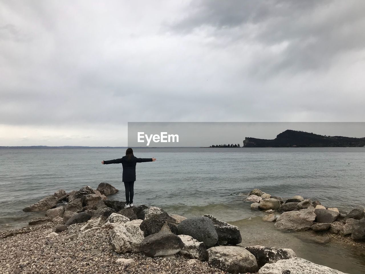 REAR VIEW OF MAN STANDING ON SHORE BY SEA AGAINST SKY