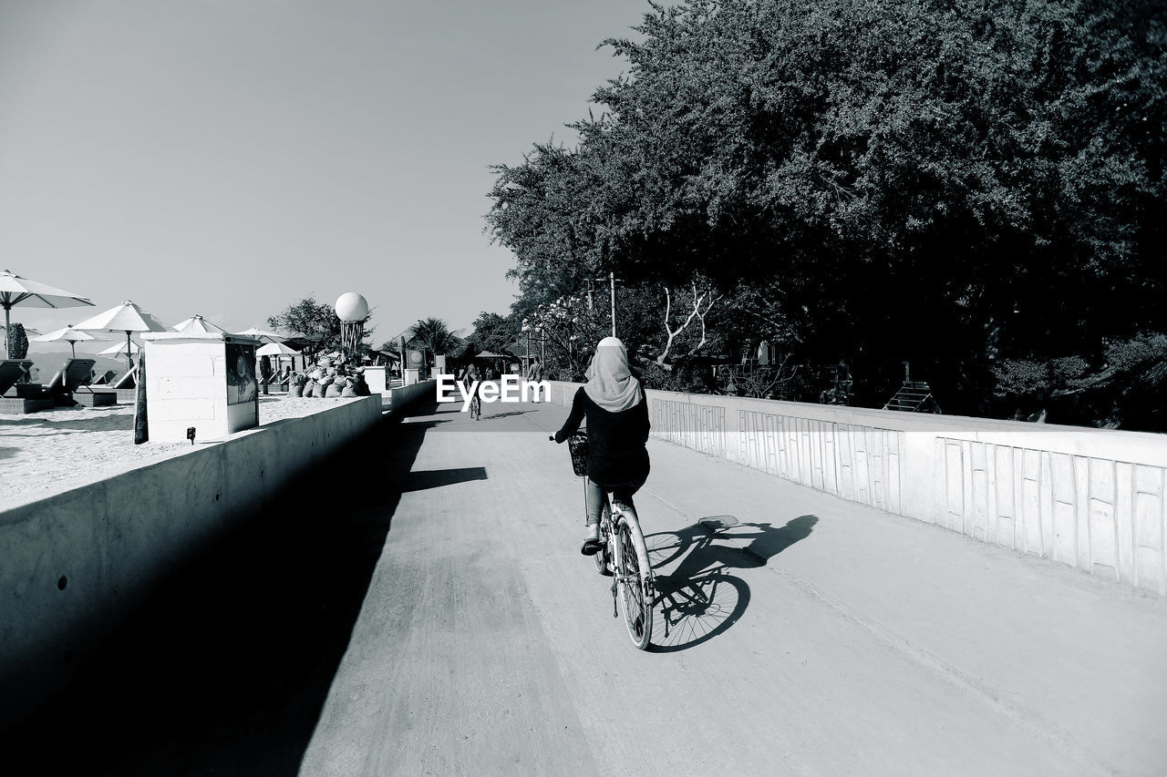 REAR VIEW OF MAN RIDING BICYCLE AGAINST SKY