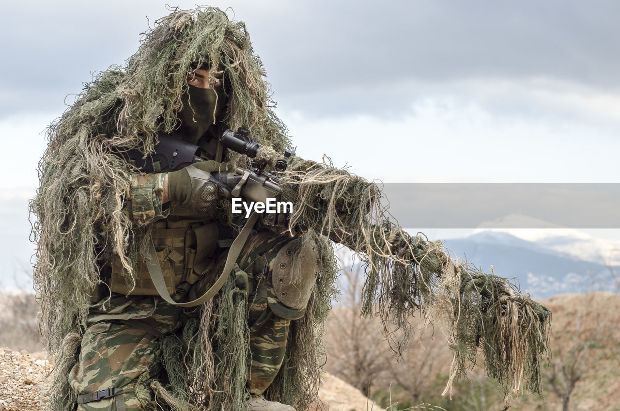 Army man in ghillie suit with rifle on field