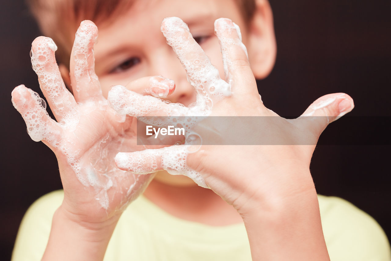 Cute boy looking at his hands with soupsuds, focus on hands